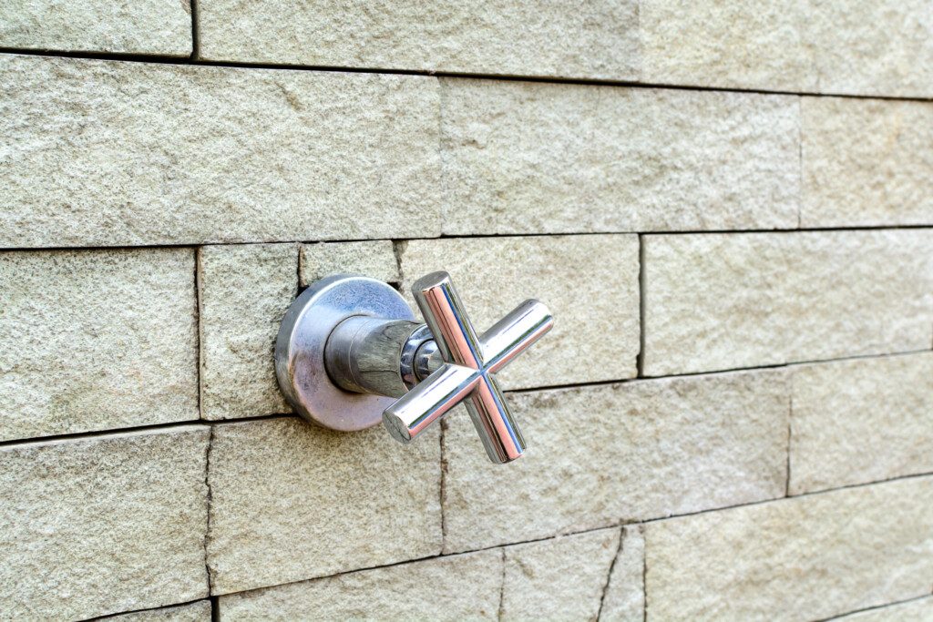 Imagem de um registro de chuveiro metálico em formato de X instalado em uma parede de tijolos 