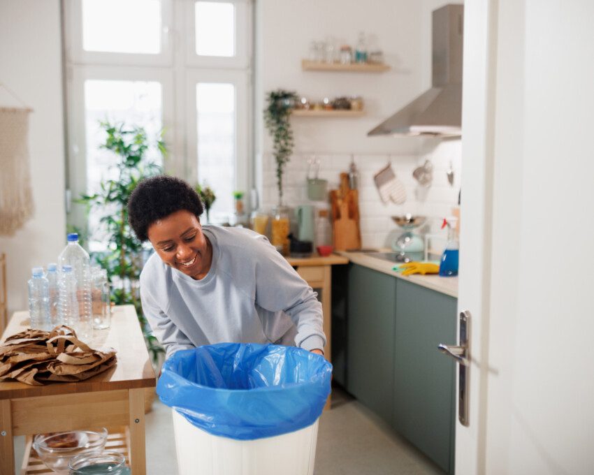 Imagem de uma mulher colocando um saco de lixo azul em uma lixeira branca na cozinha de casa