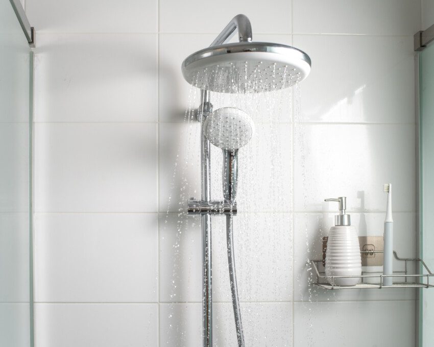Chuveiro aberto com uma ducha menor ao lado em um banheiro com revestimento branco