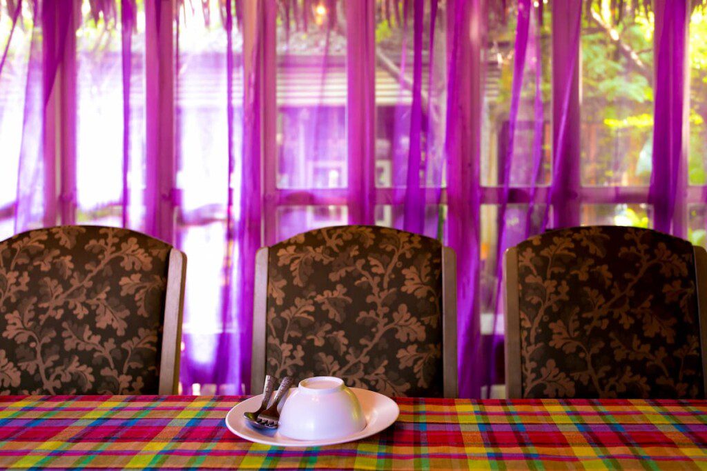 Mesa de jantar com tolha que contrasta com o tecido das cadeiras e da cortina que fica atrás. Uma boa estratégia para decoração weirdcore.
