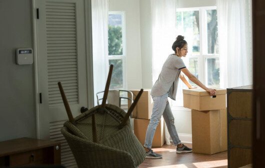 Foto que ilustra matéria sobre sair de casa mostra uma mulher em meio a caixas de mudança no cômodo de um imóvel