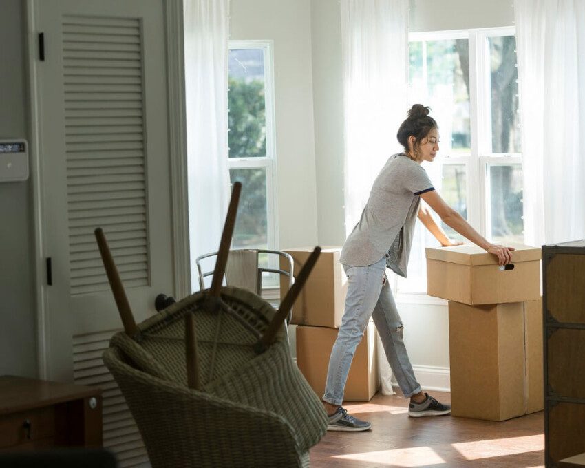Foto que ilustra matéria sobre sair de casa mostra uma mulher em meio a caixas de mudança no cômodo de um imóvel