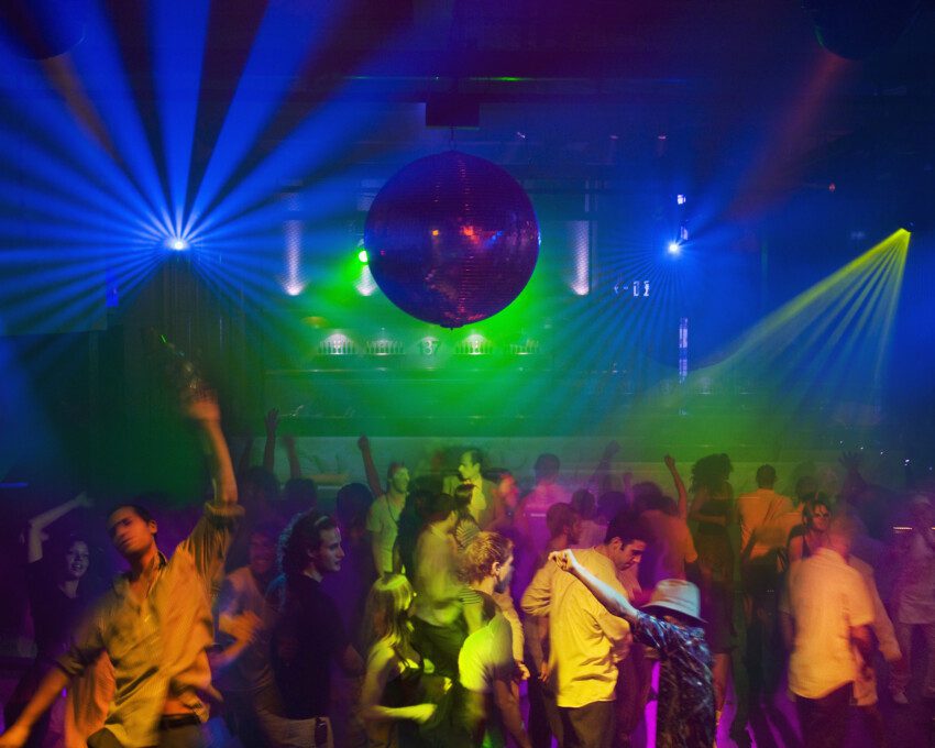 Imagem de pessoas dançando em uma balada com globo de luz e luzes verdes para ilustrar matéria sobre baladas em SP