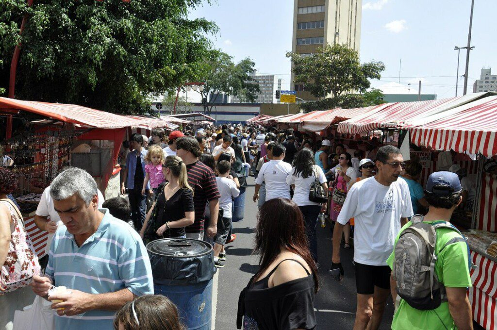 Imagem de pessoas circulando por uma via repleta de barracas para ilustrar matéria sobre as feiras em SP