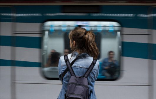 Vista traseira de uma mulher de costas com uma mochila nas costas esperando o metrô na estação para ilustrar matéria sobre a linha 6, do metrô de São Paulo