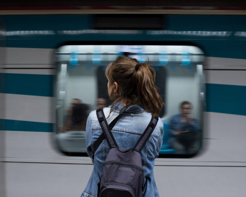 Vista traseira de uma mulher de costas com uma mochila nas costas esperando o metrô na estação para ilustrar matéria sobre a linha 6, do metrô de São Paulo
