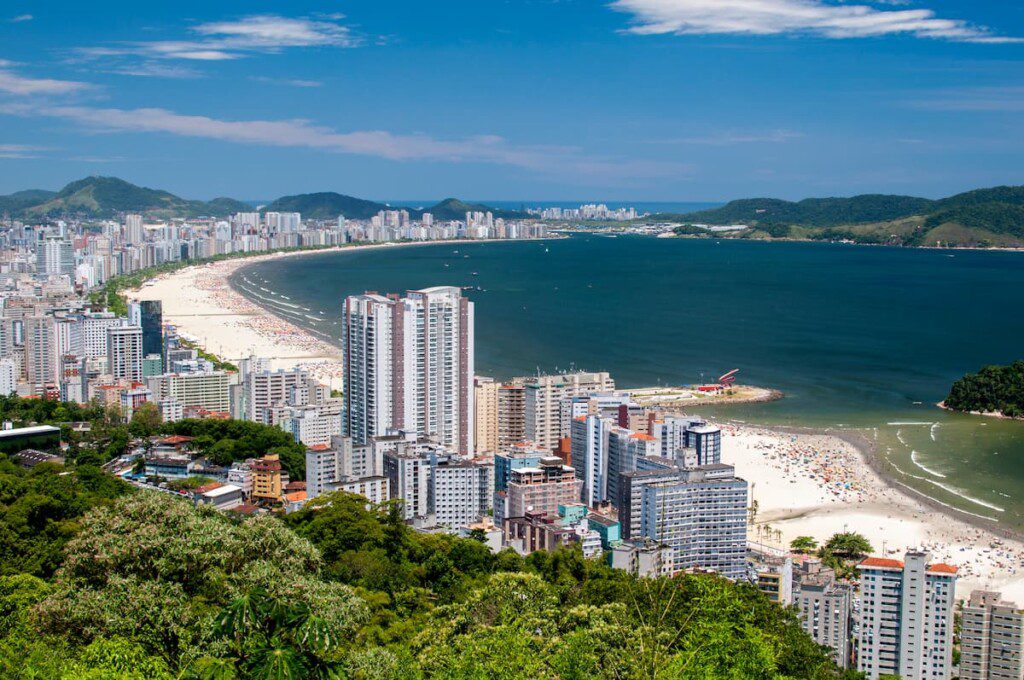 Fotografia aérea do litoral da cidade de Santos. Na imagem vemos prédios e praia.