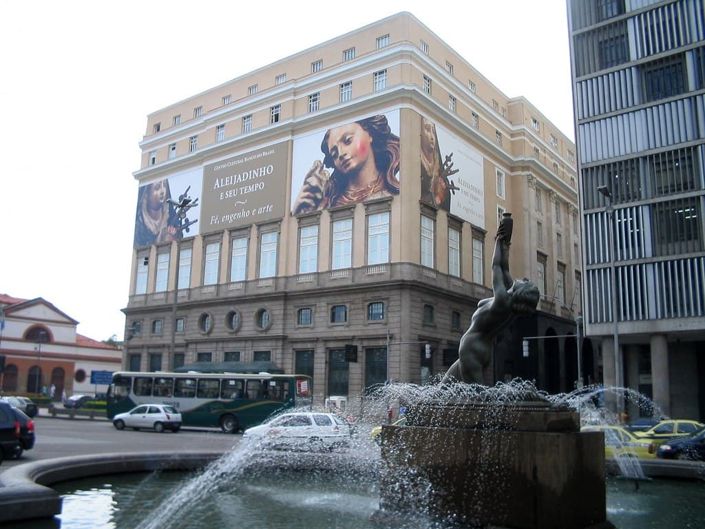 Fachada do Centro Cultural Banco do Brasil. Há uma fonte de água, com uma estátua na frente.