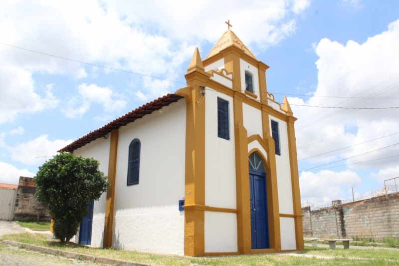 Imagem da entrada da Capela de São Sebastião que tem a cor branca, com detalhes amarelos e portas e janelas em tons azul escuro