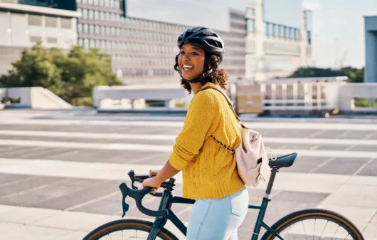 Uma mulher caminha, em uma cidade, ao lado de sua bicicleta.