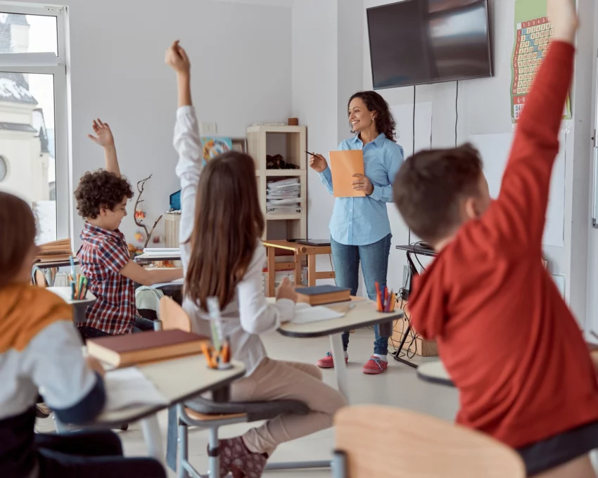 Imagem de uma sala de aula com alunos de costas sentados em carteiras em frente a uma professora para ilustrar matéria sobre as melhores escolas da Zona Oeste de SP