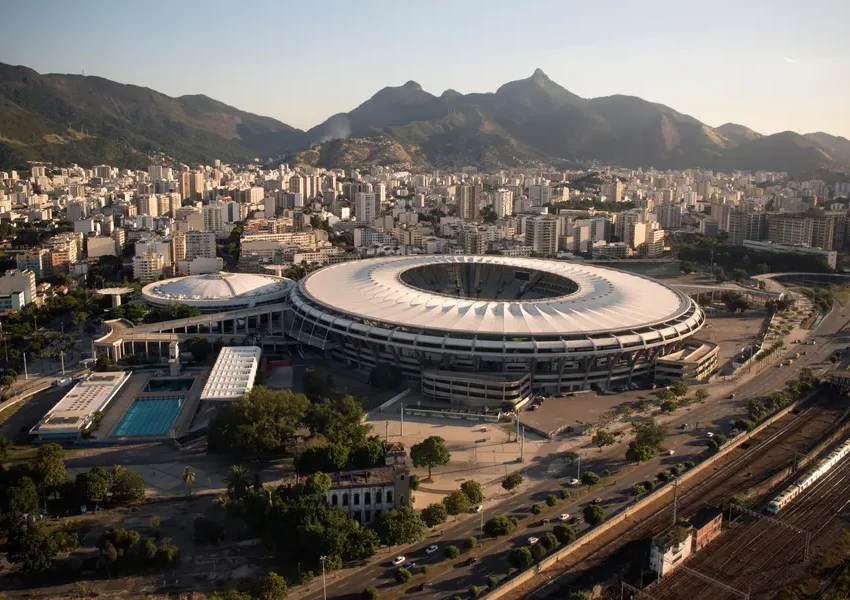 Foto que ilustra matéria sobre o estádio do Maracanã mostra o complexo onde fica a arena vista do alto, com prédios e montanhas do Rio de Janeiro ao fundo.