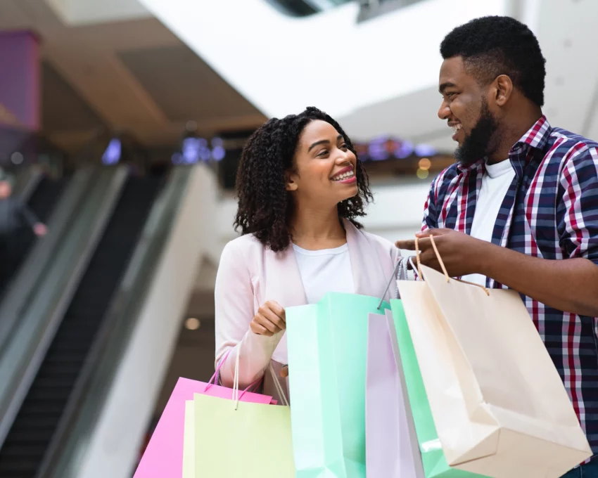 Imagem de um casal negro, composto por um homem e uma mulher, felizes com sacolas de compras nas mãos para ilustrar matéria sobre os melhores shoppings de SP