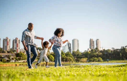 Imagem de uma família, composta por um homem, uma mulher e uma criança pequena, passeando no final da tarde em um parque para ilustrar matéria sobre o ABC Paulista