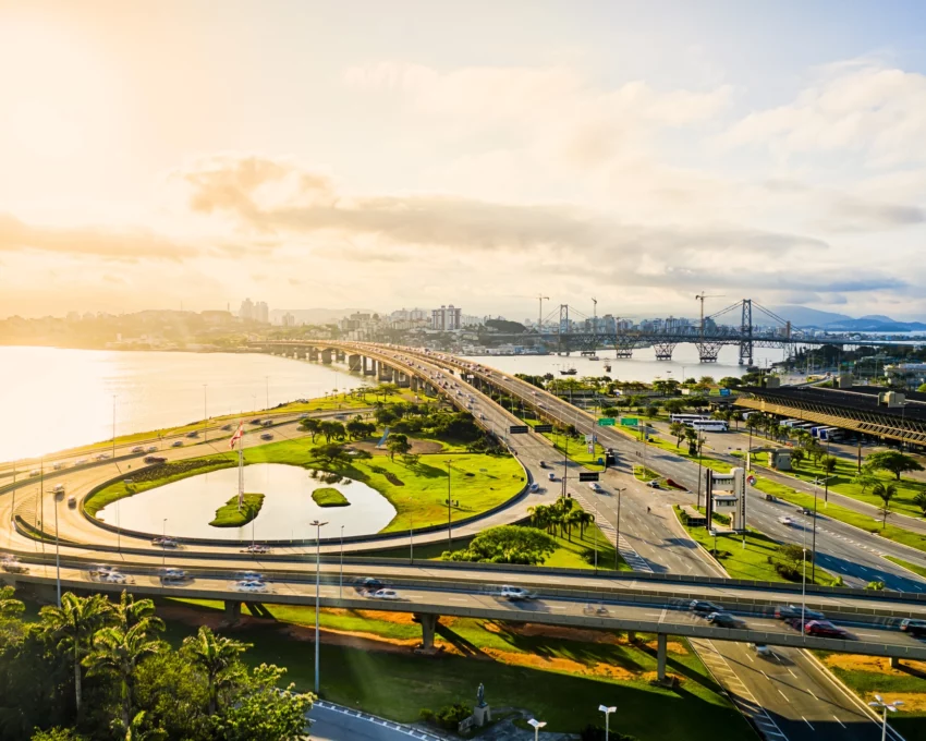 Imagem aérea de carros nos viadutos e pistas próximos ao mar durante o nascer do sol em Florianópolis para ilustrar matéria sobre cidades tranquilas para morar