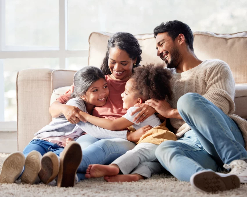 Imagem de uma família composta por um homem, uma mulher e duas crianças felizes no chão da sala para ilustrar matéria sobre o estado mais seguro do Brasil