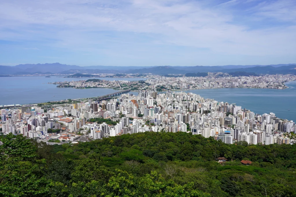  Imagem da paisagem urbana de Florianópolis, capital de Santa Catarina, mostra vegetação, prédios e o mar
