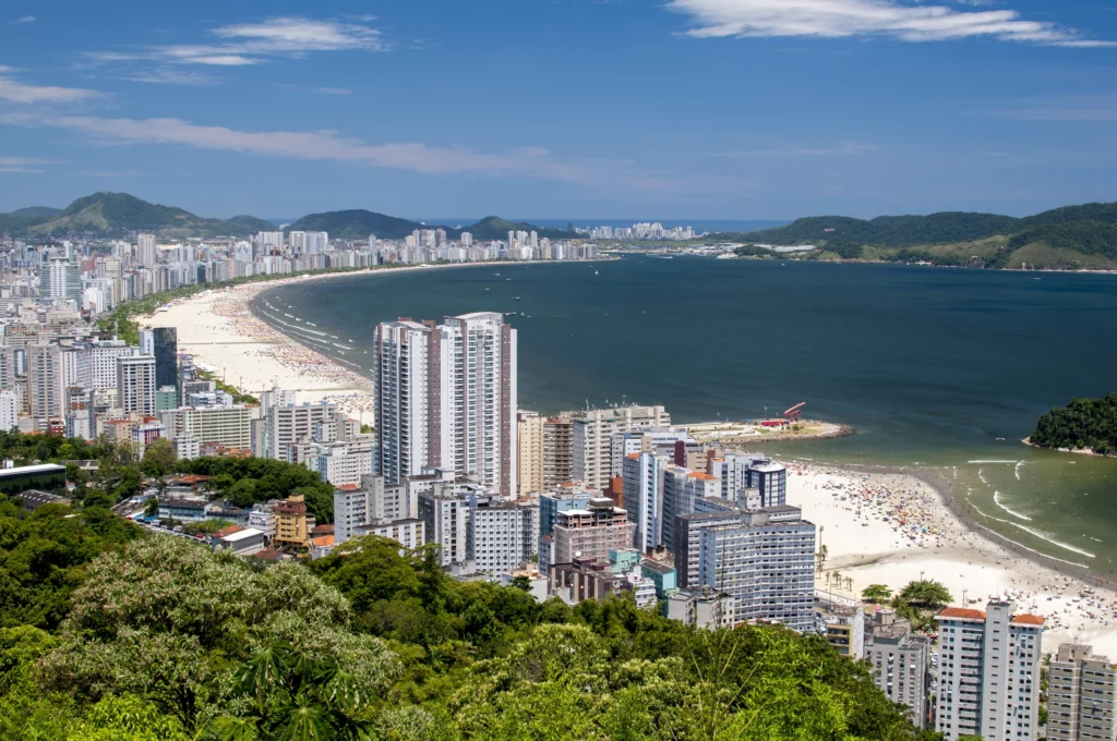 Imagem da paisagem urbana de Santos mostra prédios, faixa de areia e mar para ilustrar matéria vantagens de morar em Santos