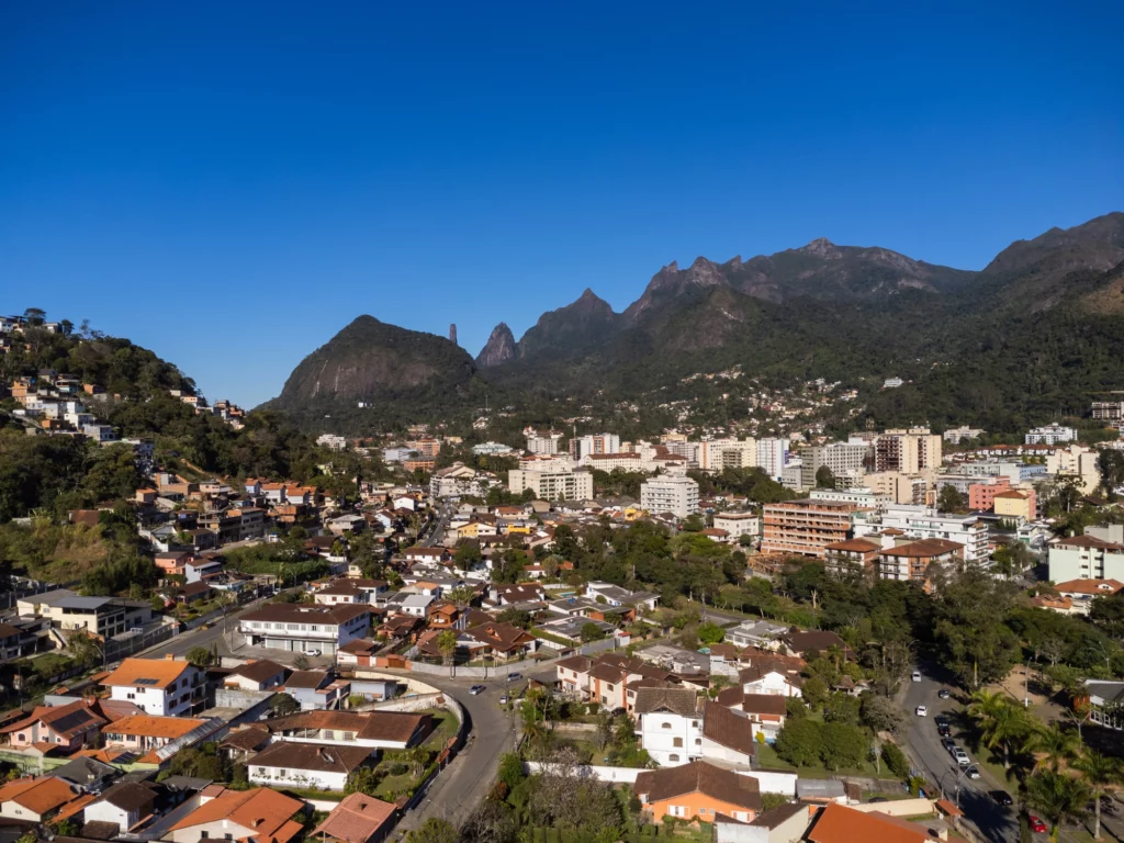 Vista aérea da cidade de Teresópolis mostra casas, prédios, montanhas e um céu azul