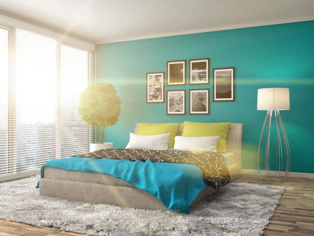 Imagem de um quarto de casal com parede azul-turquesa, cama com tons coloridos e tapete de pelo cinza para ilustrar matéria sobre cor ideal para quarto de casal