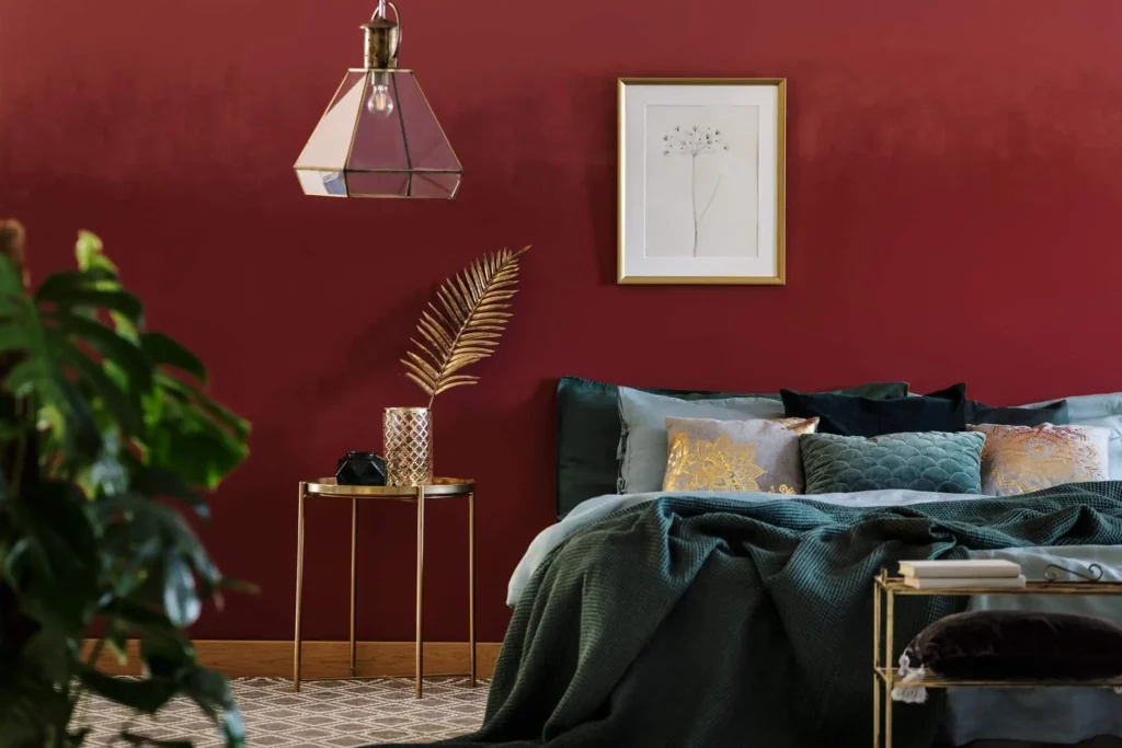 Imagem de um quarto de casal com parede vermelho-rubi e decoração em tons escuros e dourado para ilustrar a matéria sobre cores bonitas para quarto de casal