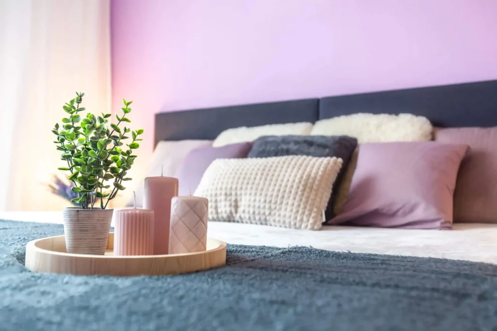 Imagem de um decoração de velas em cima de uma cama de casal e uma parede cor lavanda em segundo plano para ilustrar matéria sobre cores para pintar quarto de casal
