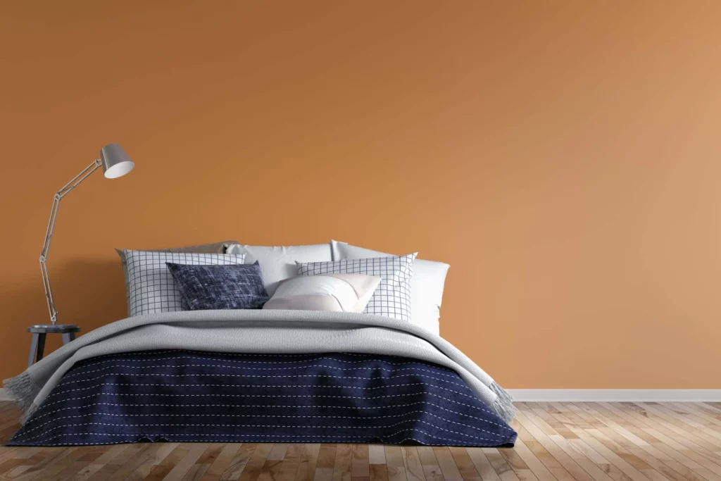Imagem de um quarto de casal com parede laranja suave e decoração minimalista em tons de cinza para ilustrar matéria sobre cores para quarto de casal simples