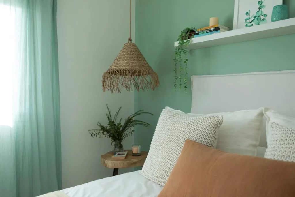 Imagem de um quarto de casal com parede verde-claro, cortina no mesmo tom e decoração com plantas para ilustrar matéria sobre melhores cores para quarto de casa