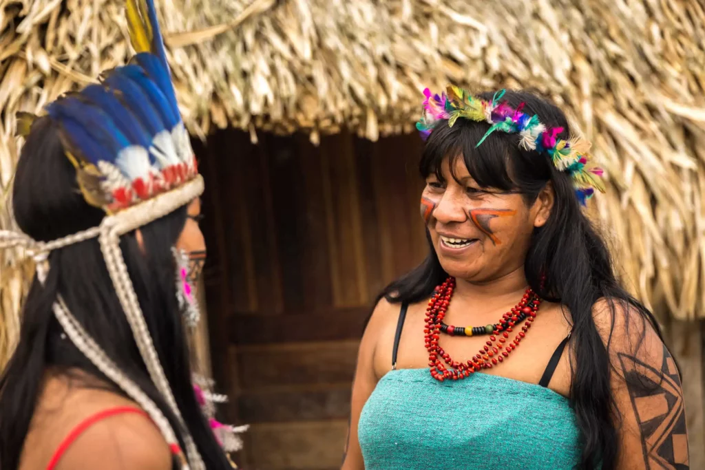 Imagem de duas mulheres indígenas da tribo Tupi Guarani conversando para ilustrar matéria sobre a umidade em cidades brasileiras