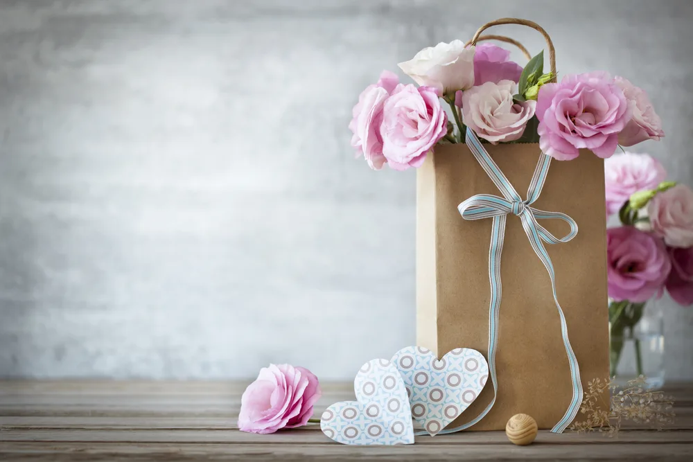Foto que ilustra matéria sobre decoração para dia das mães mostra um arranjo de flores em uma sacola de papel com um laço e corações de papel cortados (Foto: Shutterstock)