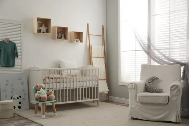 Foto de um quarto de bebê com berço, poltrona e acessórios decorativos.