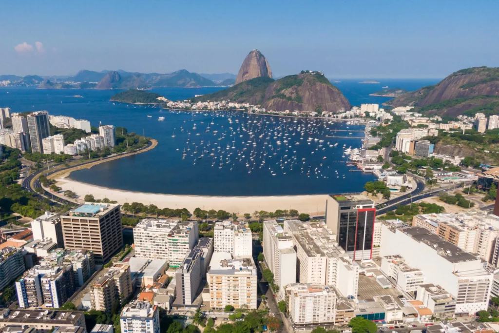 Imagem da vista aérea do bairro de Botafogo mostra Pão de Açúcar, mar, faixa de areia, prédios e vegetação para ilustrar matéria sobre o que fazer na Zona Sul do RJ